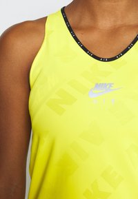 Top de tirantes amarillo de Nike con un escote redondo negro, que presenta un sutil patrón de logotipos y la palabra "AIR" en plateado metálico en la parte frontal.