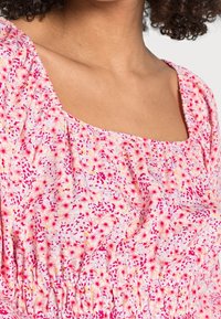 Top floreale con sfondo rosa e macchie gialle e rosse, scollo quadrato, maniche corte e un tessuto arricciato in vita.