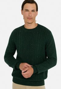 Dunkelgrüner gestrickter Pullover mit einem strukturierten Zopfmuster und mehrfarbigen Einsprengseln. Mit Rundhalsausschnitt und gerippten Bündchen und Saum.