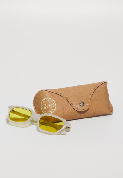 Слънчеви очила Ray-Ban с жълти лещи в прозрачна рамка, съчетани с кафяв, намачкан кожен калъф с златно лого и закопчаване с капсула.