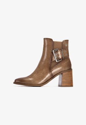 Botín de tobillo de charol marrón con punta cuadrada, detalle de hebilla lateral y tacón de madera apilada. Textura elegante y suave.