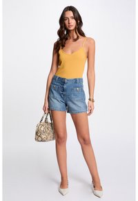 Yellow ribbed tank top with thin straps, high-waisted denim shorts, beige snake-print handbag, and pointed-toe light gray heels.