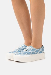 Blue canvas sneakers with a geometric white pattern, white laces, and a thick white sole. Low-top design, textured fabric.