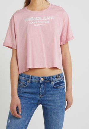 T-shirt rose cropped avec des manches courtes, ornée d'un logo blanc sur le devant. Associé à un jean en denim bleu déchiré.