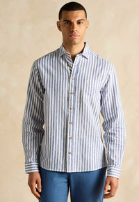 Zilā un baltā lina krekliņa ar svītrām, kuram ir garas piedurknes, krūšu kabata un brūni pogu akcenti. Pielāgota piegriezuma ar izliekto apakšmalu.