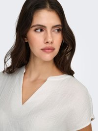 Wit, gestructureerd topje met een V-hals en korte mouwen. Zachte, lichte stof met een subtiel geplooid patroon.