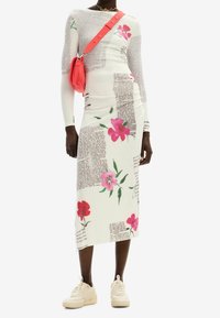 Robe blanche à manches longues avec imprimés floraux et design textuel, associée à un petit sac rose. Modèle portant des baskets beiges.