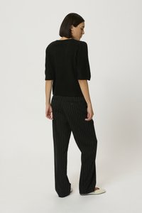 Pulover negru din tricot cu mâneci scurte și largi. Asortat cu pantaloni negri cu dungi verticale. Ținuta are o croială relaxată și o textură netedă.