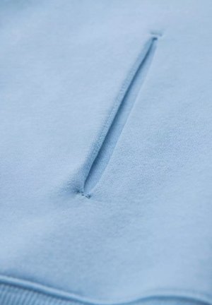 Světle modrý svetr s texturovaným, jemným povrchem, který má na přední straně malou vertikální kapsu. Hladká tkanina s jemným prošíváním.