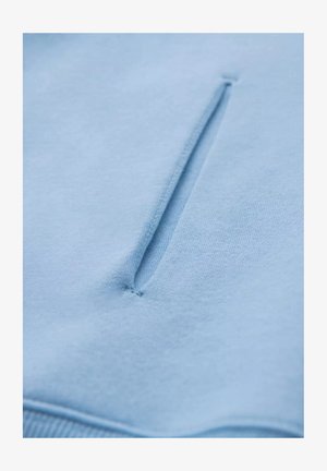 Ljusblå sweatshirt med en strukturerad, mjuk yta, som har en liten, vertikal ficka fram. Slät tyg med subtila sömmar.