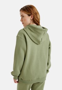 Olivegrüner Hoodie aus weichem Material, mit einer Kängurutasche und verstellbarer Kapuze, sowie gerippten Bündchen und Saum.