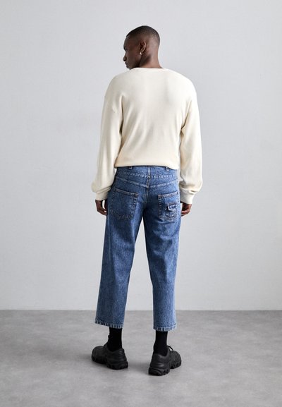 Cream ribbed sweater, blue denim jeans with a relaxed fit, and black chunky shoes. Rear view, with side and back pocket detailing visible.