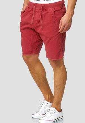 Shorts en coton rouges avec une taille à cordon de serrage, dotés de poches latérales et d'un ourlet effiloché. Associés à des baskets blanches.