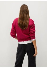 Pull en tricot fuchsia à manches longues, col rond et poignets côtelés, associé à un jean noir taille haute. Design simple et texturé.