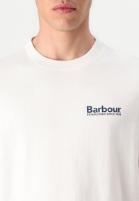 Witte katoenen t-shirt met een ronde hals, voorzien van een marineblauw bedrukt logo "Barbour" en "GESTICHT SINDS 1894" op de borst.