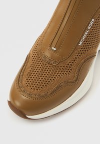 Rjava športna obutev z zgornjim delom iz teksturiranega pletiva in gladkimi usnjenimi poudarki. Opremljena je z zadrgo za zapiranje in belo gumijasto podplatom.