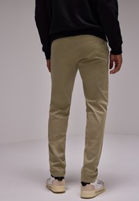 Light khaki cotton pants with a slim fit, featuring subtle texture and a back pocket, worn with white and beige sneakers.