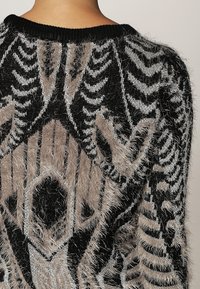 Maglione a maglia nero e beige fuzzy con motivi geometrici, dotato di scollatura a girocollo e design testurizzato.