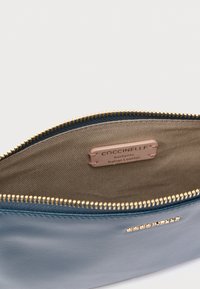 Modrá kožená taštička se zlatým zipem, s béžovým vnitřkem a štítkem s nápisem „Coccinelle, Pravá italská kůže.“