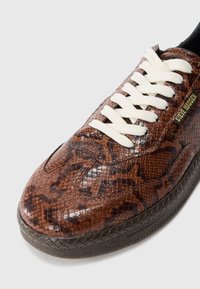 Brune snakelskinsneakers med hvide snørebånd og sort gummisål, udstyret med et lille "Steve Madden"-mærke på siden.
