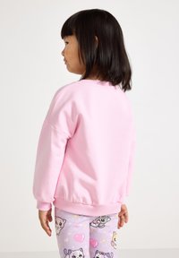 Felpa rosa chiaro con scollatura e polsini a coste, caratterizzata da una vestibilità comoda. Abbinata a leggings a fantasia con animali dei cartoni animati e cuori.