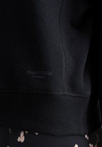 Felpa nera con orlo e polsini a coste. Presenta un tessuto testurizzato e un piccolo logo in rilievo vicino al fondo.