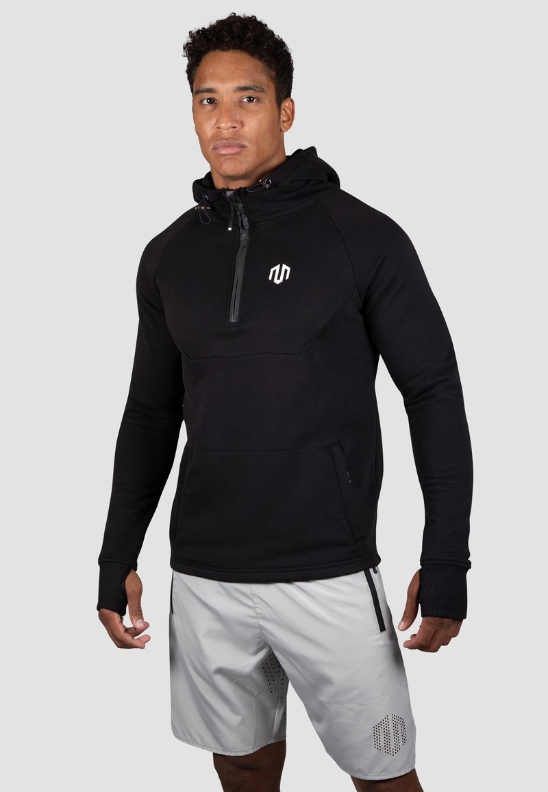 Czarny rozpinany hoodie z zamkiem na szyi, z przednią kieszenią i logo. Noszony z jasnoszarymi krótkimi spodniami o perforowanym wzorze.