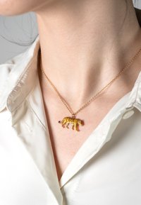 Zelta tonalitātes kaklarota ar dzeltenu leopardu piekariņu, kura virsmā ir melnas plankumi, atpūšas uz gludas, gaišas krāsas krekla apkakles.