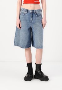 Pantalones cortos de mezclilla azul claro con un corte holgado, con una cintura alta, cinco bolsillos y dobladillo deshilachado, combinados con botas de combate negras.