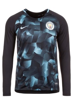 Czarna koszulka sportowa z długim rękawem z niebieskim geometrycznym wzorem, logo Nike po lewej stronie klatki piersiowej i emblemat klubu piłkarskiego Manchester City po prawej stronie klatki piersiowej.