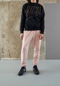 Czarna bluza Nike z wielokolorowym logo, połączona z jasnoróżowymi spodniami dresowymi. Czarne sneakersy z turkusowymi akcentami i różowymi detalami.