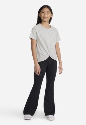 Světle šedé tričko s krátkým rukávem a uzlovým detailem vpředu, kombinované s černými zvonovými kalhotami a bílými teniskami. Hladká, měkká textura látky.