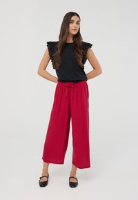 Top nero con maniche in pizzo arricciato, abbinato a pantaloni a gamba larga rossi con vita regolabile e scarpe nere flat.