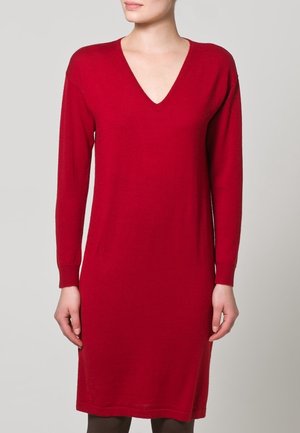 Robe en maille rouge à manches longues avec un décolleté en V profond. La coupe est ajustée et la robe arrive juste au-dessus du genou, réalisée dans un tissu doux et texturé.