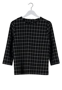 Černý top s dlouhým rukávem a bílým mřížkovým vzorem zavěšený na bílém ramínku na bílém pozadí.