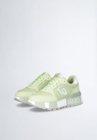 Sneaker verde chiaro realizzati in materiali mesh e suede, con un logo bianco e una suola spessa e texturizzata. I dettagli includono un tallone bianco.