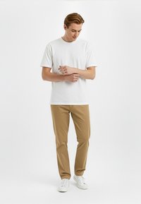 T-shirt bianca in cotone a maniche corte, abbinata a chinos beige e sneakers bianche. Texture liscia, design semplice e colori neutri.