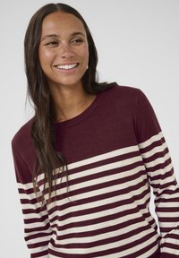 Pull rayé bordeaux et crème avec un col rond et des manches longues. Texture tricot douce, présentant des rayures horizontales alternées.