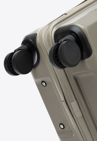 Valigia rigida beige con superficie testurizzata; presenta due ruote nere attachate alla base e una cerniera sul lato.