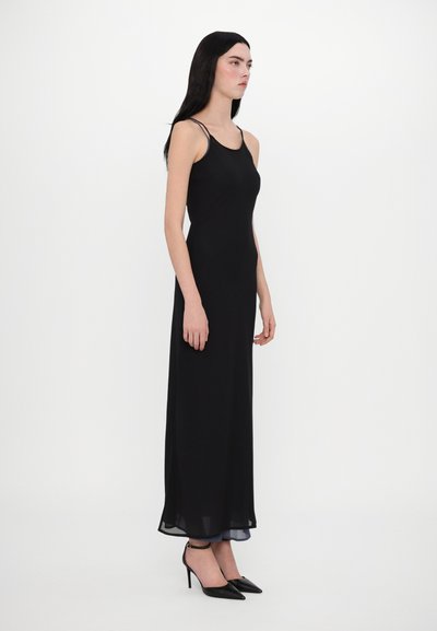 Rochie maxi neagră, ajustată, cu bretele subțiri, material fluid și hem transparent. Modelul este asociat cu pantofi cu vârf ascuțit negri. Design simplu.