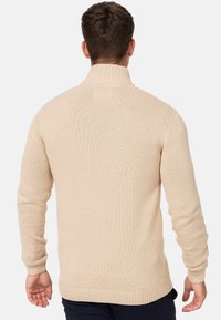 Pull beige en tricot avec un col montant, des poignets et un ourlet côtelés. Présente un motif texturé et une silhouette ajustée.