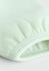 Tissu vert clair avec une texture douce. Présente un poignet élastique avec des coutures côtelées et une couture lisse pour plus de durabilité.