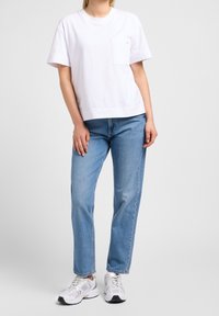 Wit katoenen T-shirt met korte mouwen en een borstzakje, gecombineerd met lichtblauwe recht gesneden jeans en witte sportieve sneakers.