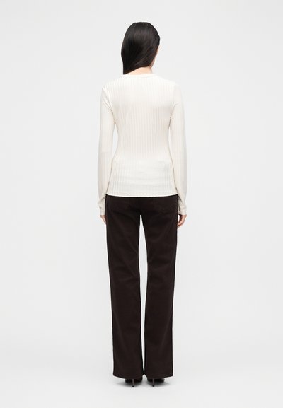 Μπλούζα με μακριά μανίκια, ριμπ ύφανση, σε ανοιχτό μπεζ χρώμα με στρογγυλή λαιμόκοψη, συνδυασμένη με καφέ παντελόνι ψηλόμεσο, με ευθεία γραμμή. Ύφασμα με ομαλή υφή.