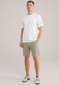 Balta kokvilnas T-kreklu, īsām piedurknēm, apvienots ar olīvzaļām šortiem, virs ceļgala. Melni un balti sporta apavi noslēdz šo apģērbu.