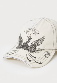 Baseball cap in cream canvas with black eagle graphic, distressed brim, and stitched details. Features "Diesel" label above the design.