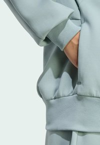 Svetlozelené mikiny s rebrovanými manžetami a lemom, s voľným strihom a detailom postranných vreciek. Mäkká, hladká textúra tkaniny.