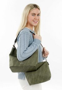 Olivgrüne Schultertasche mit weicher Textur, die ein lässiges Design aufweist und über einen abnehmbaren Tragegurt verfügt. Logo auf der Vorderseite sichtbar.