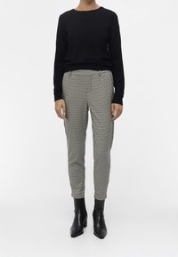 Pull noir à manches longues associé à un pantalon beige et noir à carreaux bien taillé. Complété par des bottines noires et une silhouette ajustée.