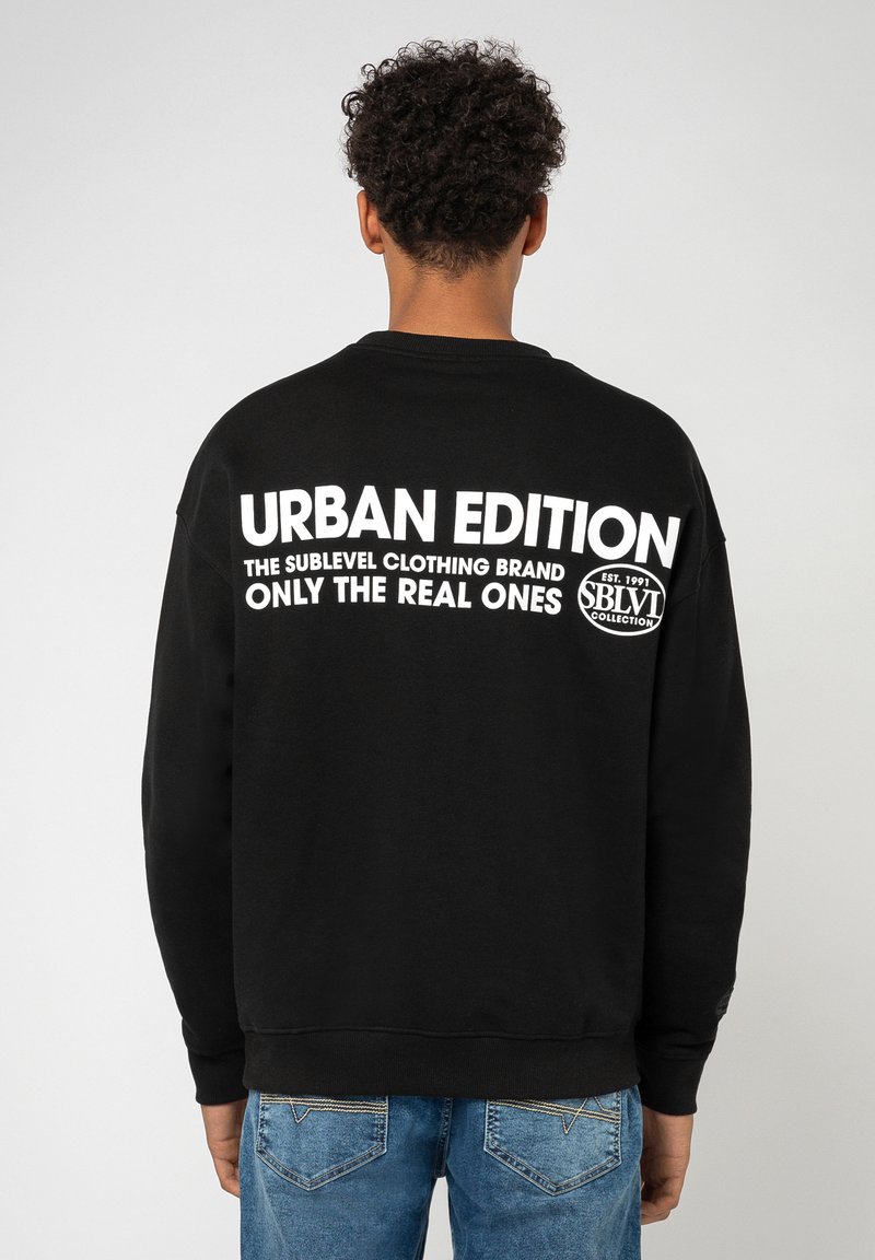 Schwarzes Sweatshirt mit weißem Text auf dem Rücken, der "URBAN EDITION" liest, mit Rundhalsausschnitt, langen Ärmeln und gerippten Bündchen.